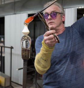 Tim Burke, an artisan glassmaker, uses tools to mold glass into a decorative object.
