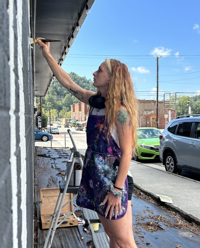 Kandee Wallace painting a LOVE mural in St. Paul on gray building.