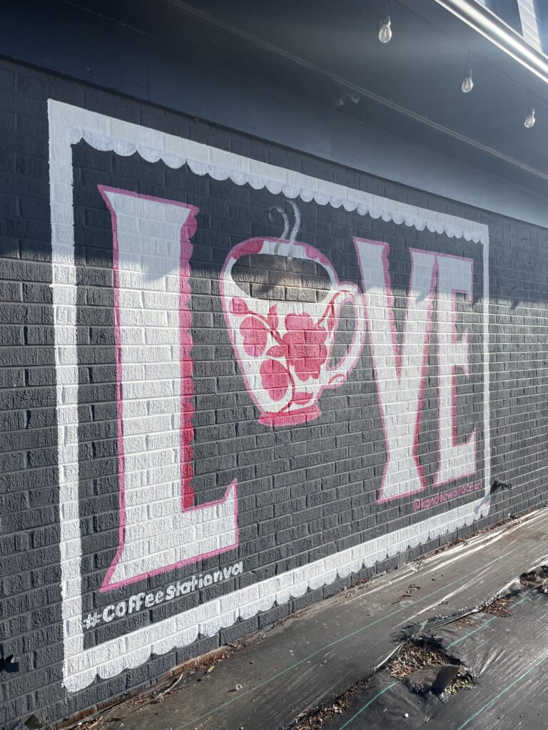 A white and pink LOVE mural with a coffee cup in place of the O on a gray building.